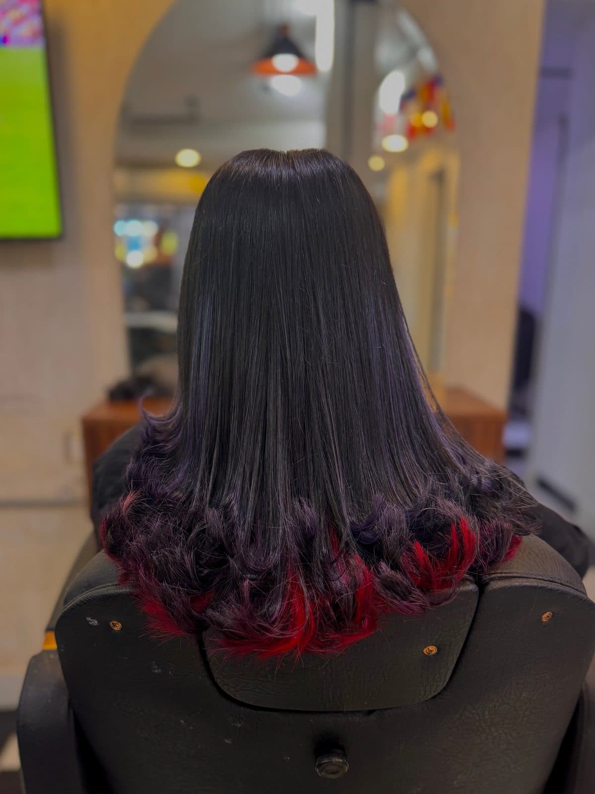 Cabello negro liso con las puntas rojas, visto de espaldas en el salón.